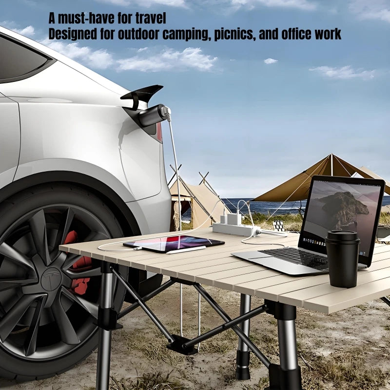 Portable folding table set up outdoors next to a car with camping and work equipment.